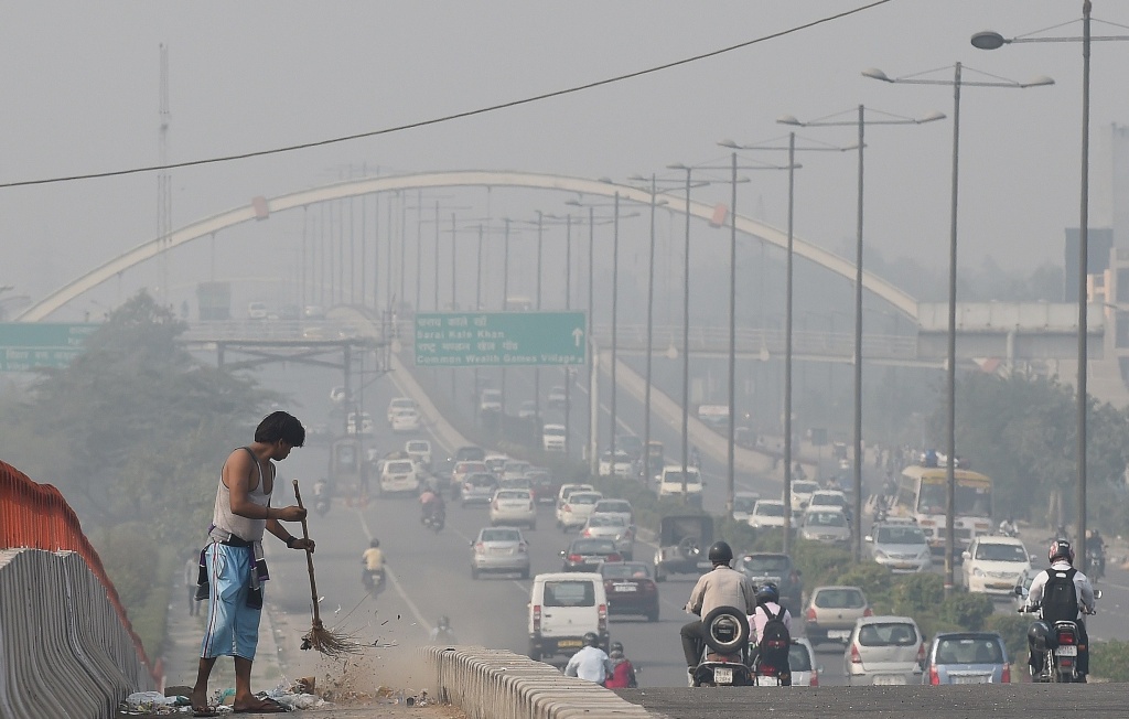 A sweeper working beside a smog filled road.